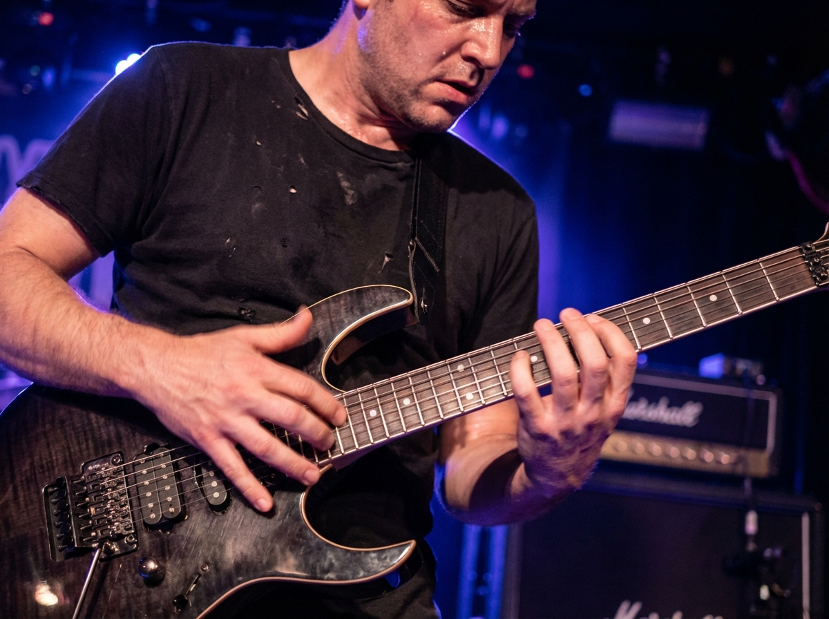 Electric guitar player performing 8-finger tapping technique with both hands fully on the fretboard showing all active fingers across a wide interval span in pentatonic scale position